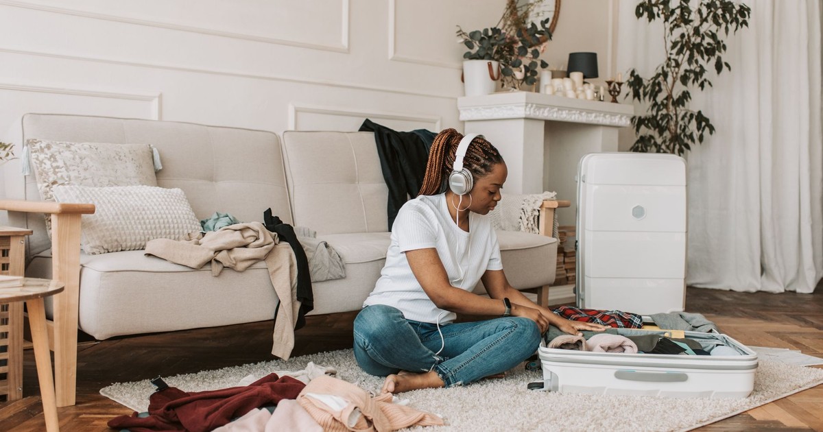A woman with headphones packing a suitcase in her stylish living room, preparing for travel.