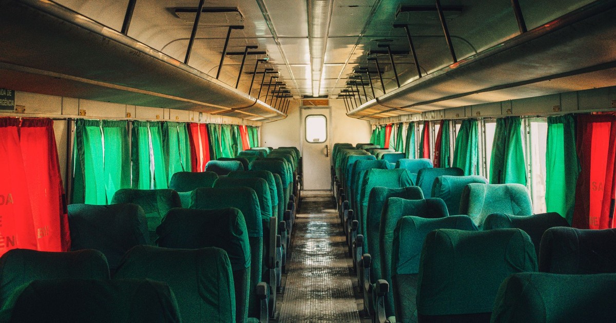 Interior of an empty train carriage with green seats and colorful curtains.