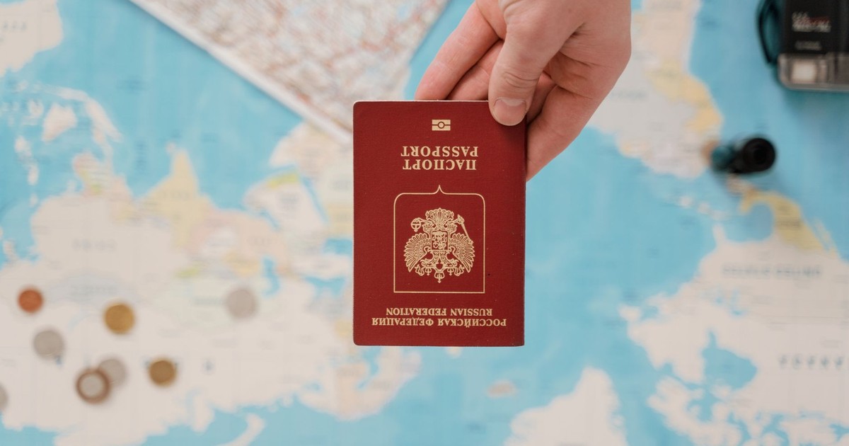 A hand holding a Russian passport above a travel-themed map, capturing world travel concepts.