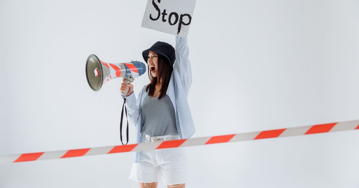 Woman holding a stop sign and megaphone while protesting in a studio setting.