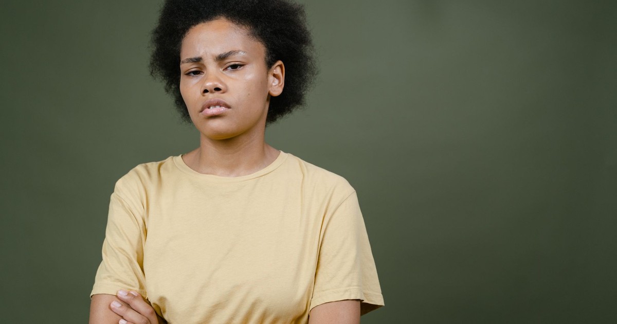 Expressive portrait of a woman with afro hair and yellow shirt against a green background.