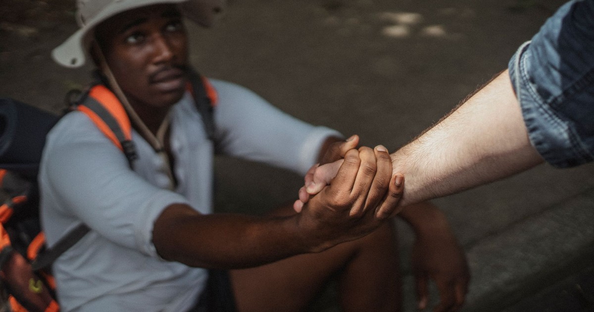 From above of crop homosexual black man in casual clothes holding hand of anonymous partner on pavement in daylight