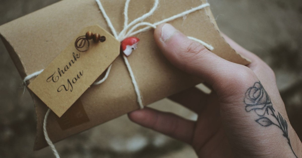 Close-up of a hand holding a thank you gift adorned with a rose tattoo, conveying a personal touch.