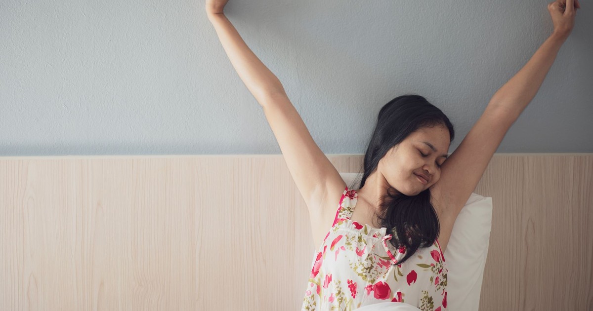 A woman joyfully stretching her arms while waking up in bed, feeling refreshed and energized.