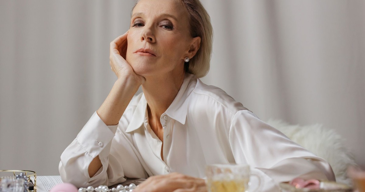 A poised senior woman in a white shirt enjoying tea, surrounded by elegant pearls.