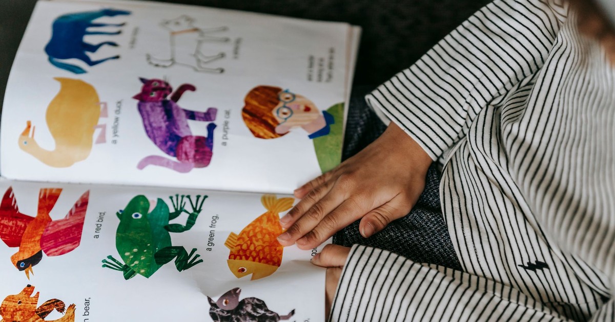 From above of crop anonymous child reading interesting book with colorful pictures of different animals