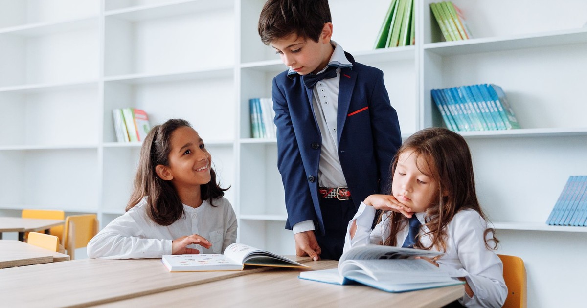 Three children engaging in reading and studying activities at a library table with bookshelves.