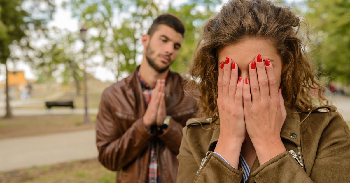 A young man apologizes while a woman covers her face, set in an outdoor park.