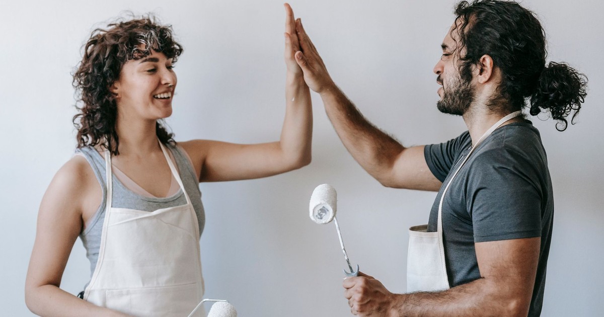 Happy couple high-fiving during home painting project, celebrating teamwork and renovation success.