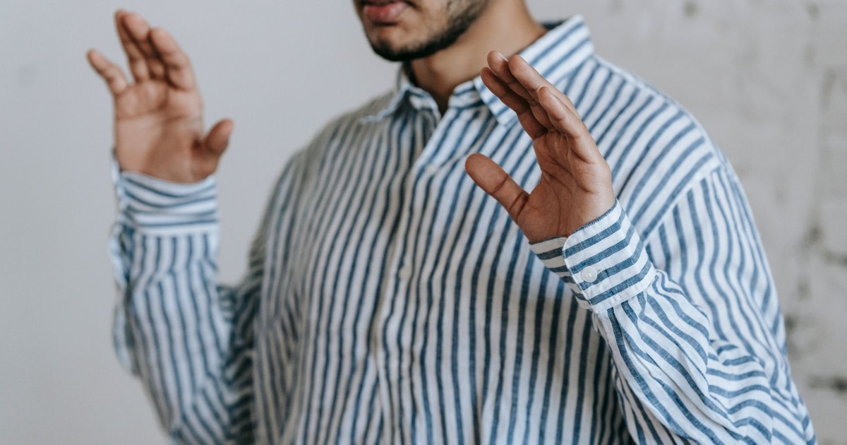 Adult man in a striped shirt praying indoors, hands raised in a traditional Islamic gesture.