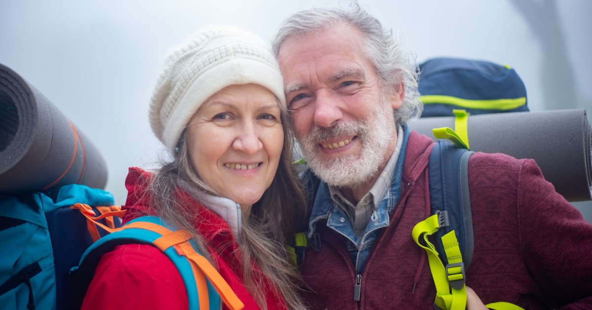 Senior couple hiking with backpacks, smiling in the outdoor misty environment of Portugal.