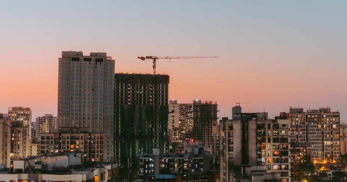 Cityscape view with buildings and a construction crane at sunset, highlighting urban development.