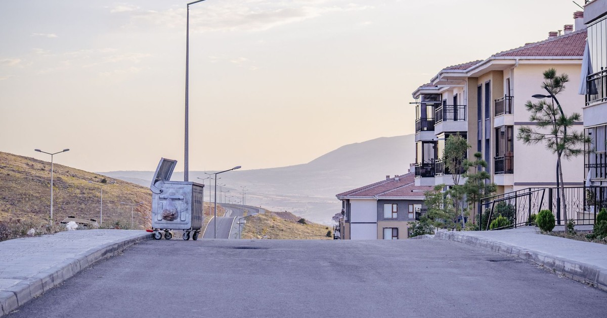 A quiet suburban street view with modern apartment buildings and a trash bin under a cloudy sky.