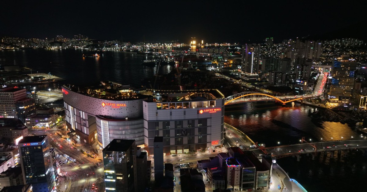 Aerial night view of Busan, South Korea featuring Lotte Mall and iconic bridges.