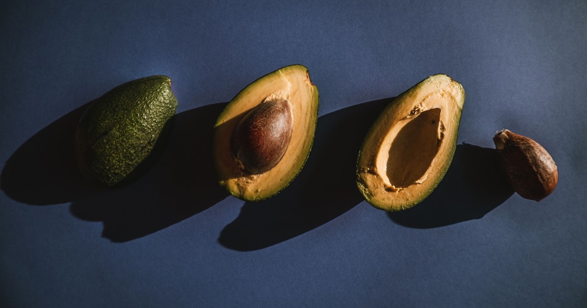 Overhead view of fresh avocados, halved and whole, with shadow play on a dark surface.