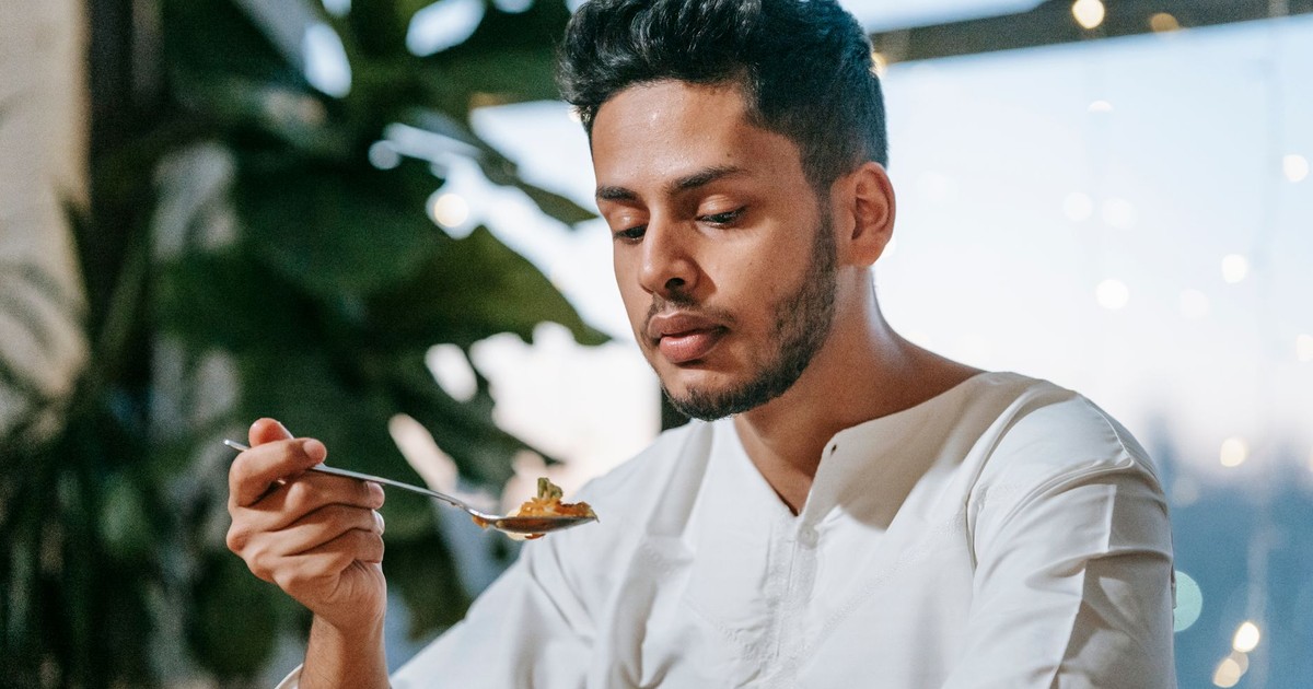 A man in traditional Islamic clothing eating indoors with string lights decor.
