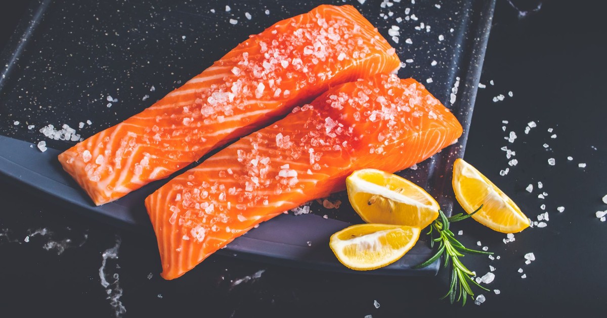 Close-up of raw salmon fillets garnished with salt, lemon wedges, and rosemary on a baking tray.