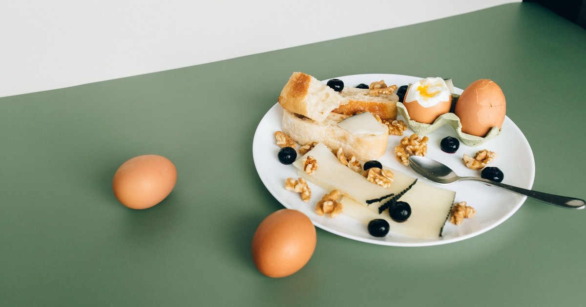 Plate of cheese, boiled eggs, bread, walnuts, and blueberries for a hearty breakfast.