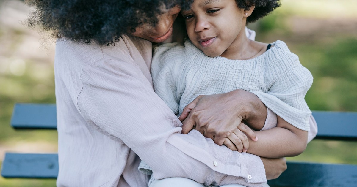 Tender moment between a mother and daughter embracing on a park bench.