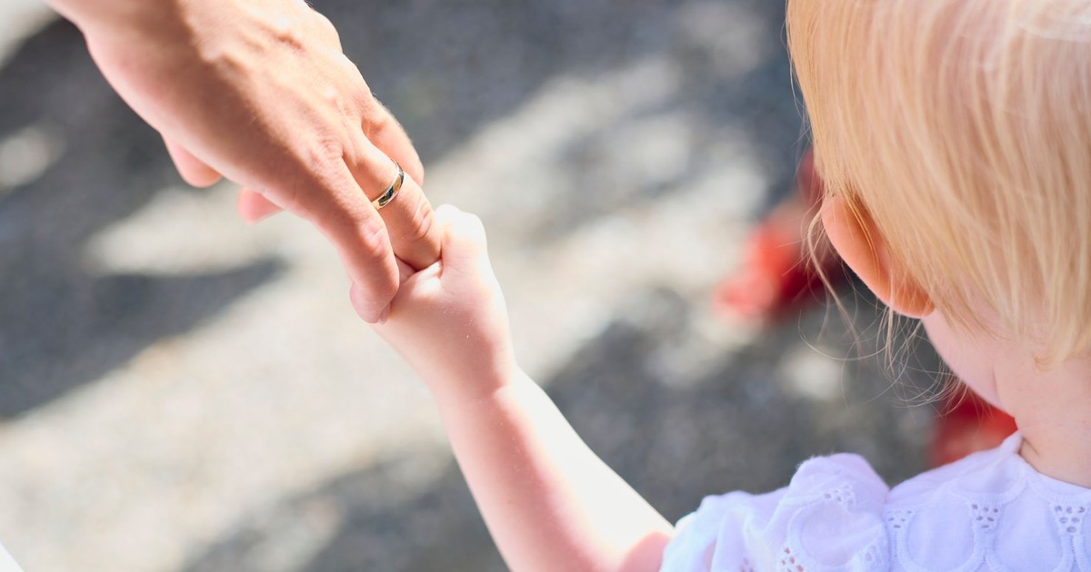 Blonde child holding parent's hand outdoors, symbolizing love and protection.