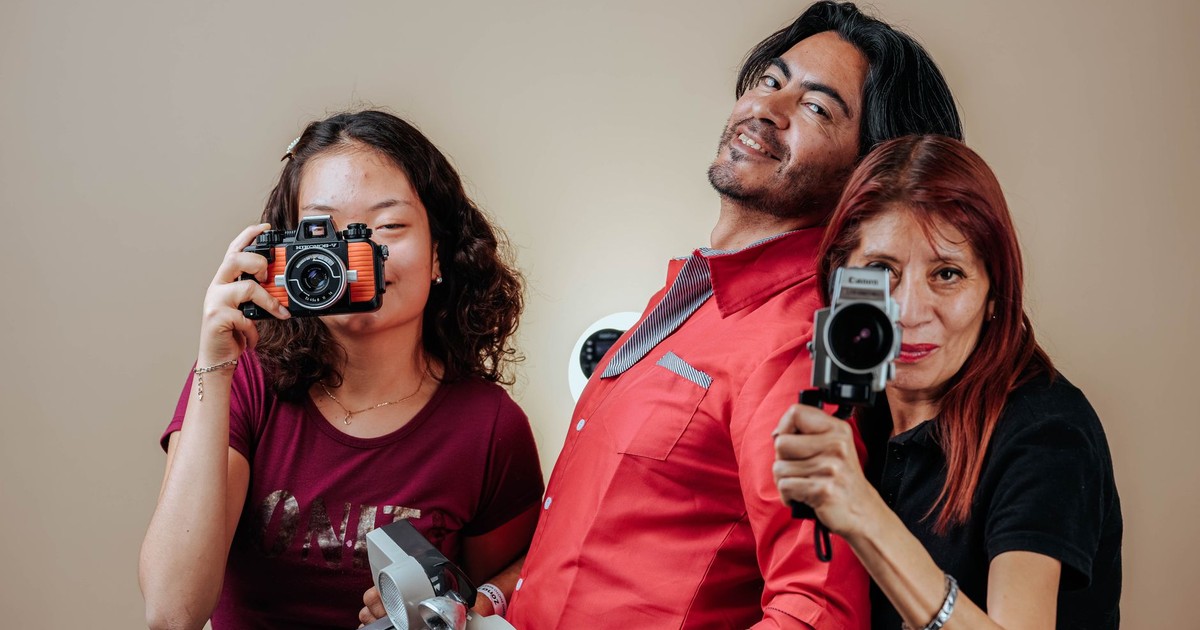 Three people posing with vintage cameras in a studio setting.
