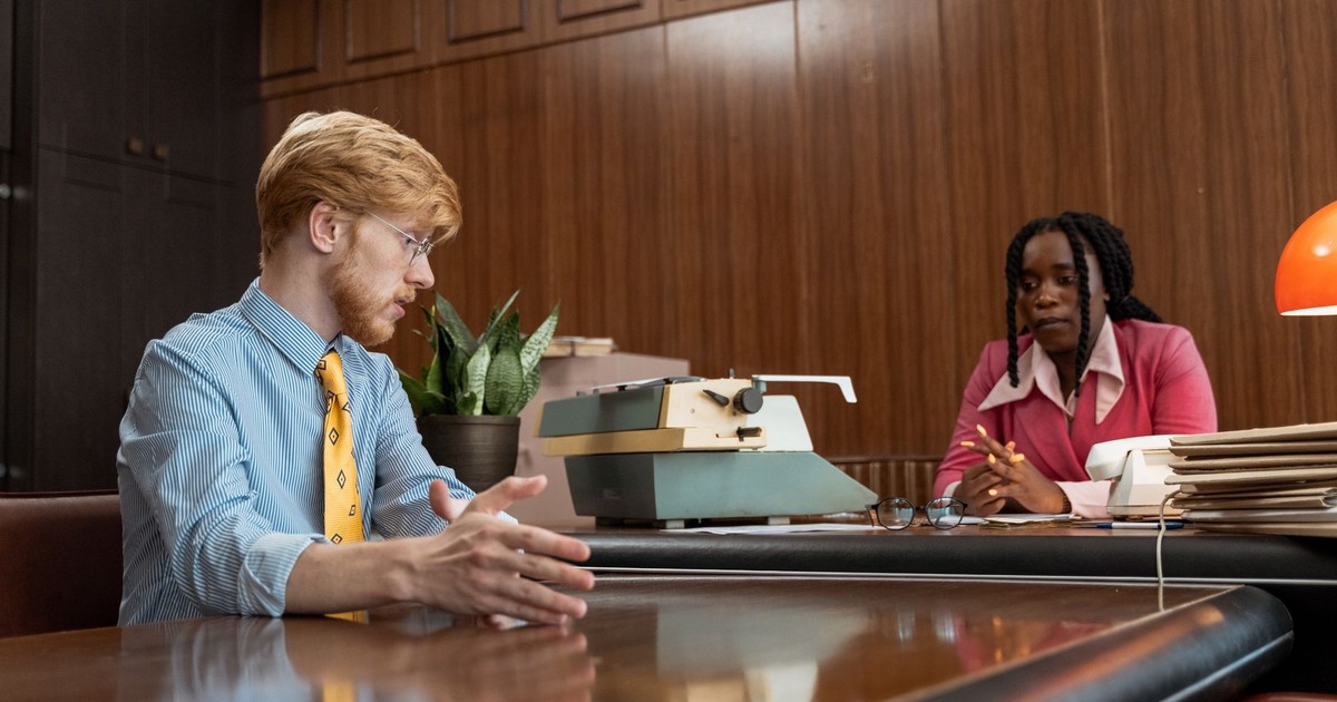 Retro office with two professionals discussing over a desk and typewriter.