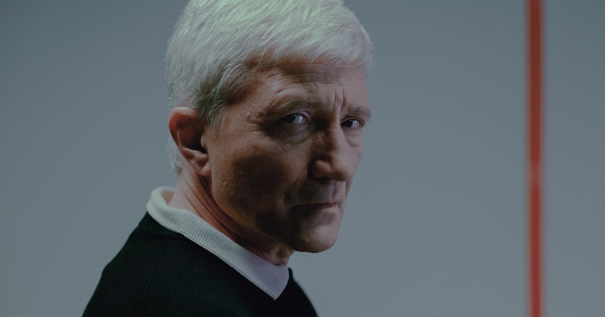 Close-up portrait of a serious senior man in a black shirt indoors.