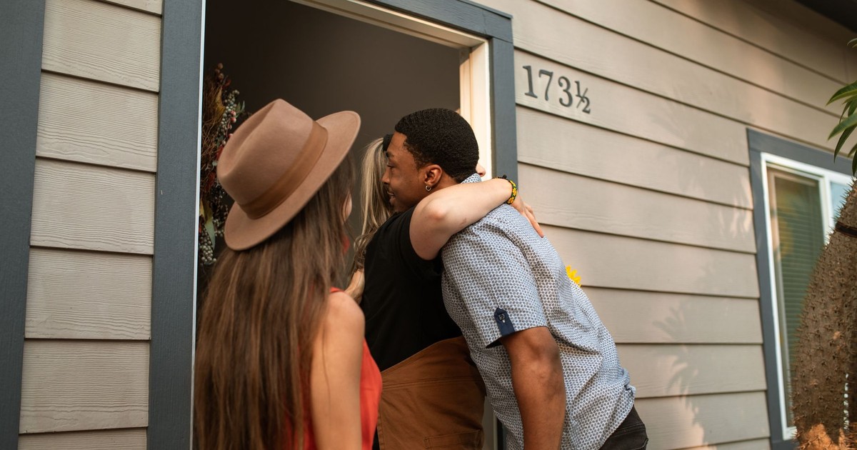Three adults warmly embrace at a doorway, exuding friendship and connection.