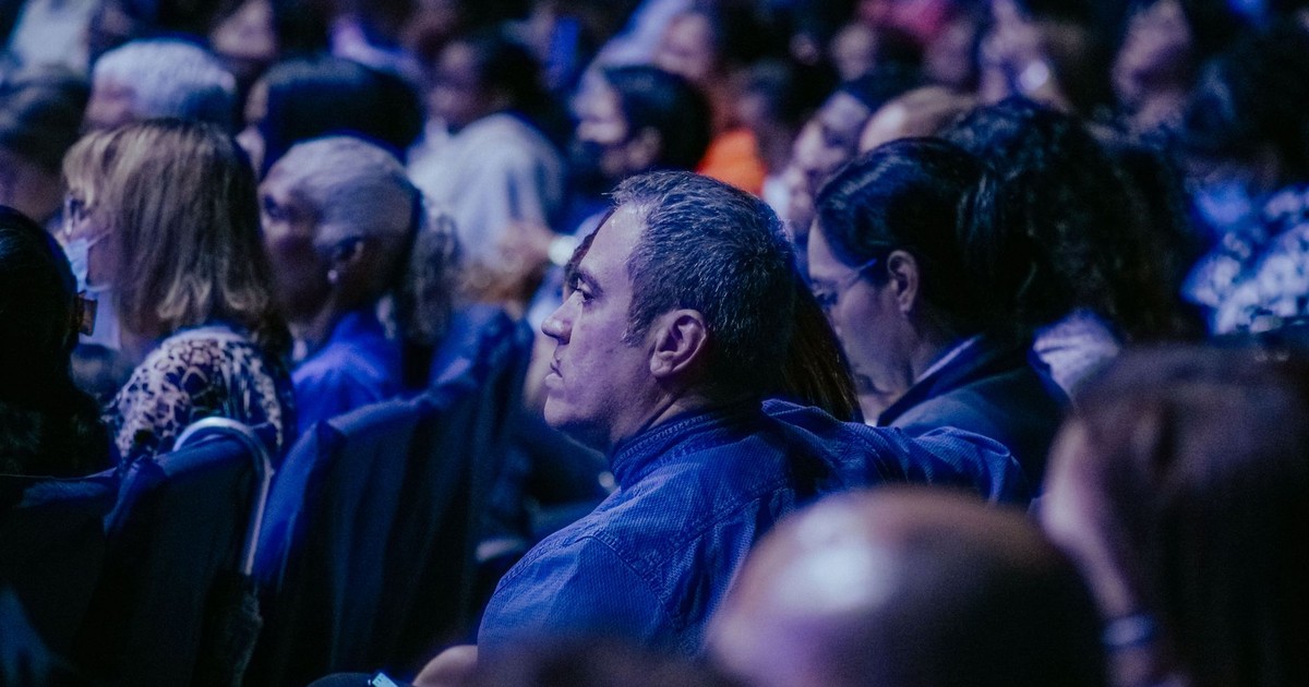 A large, diverse audience attentively listens during an indoor event.