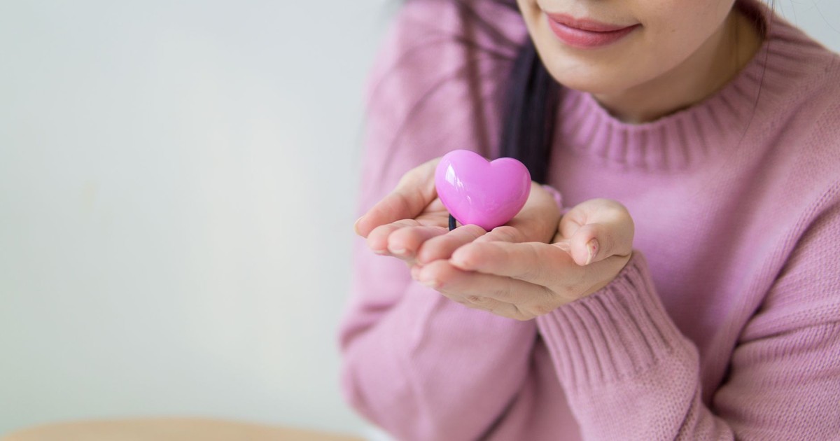 A woman in a pink sweater holding a pink heart-shaped toy, symbolizing love and kindness.