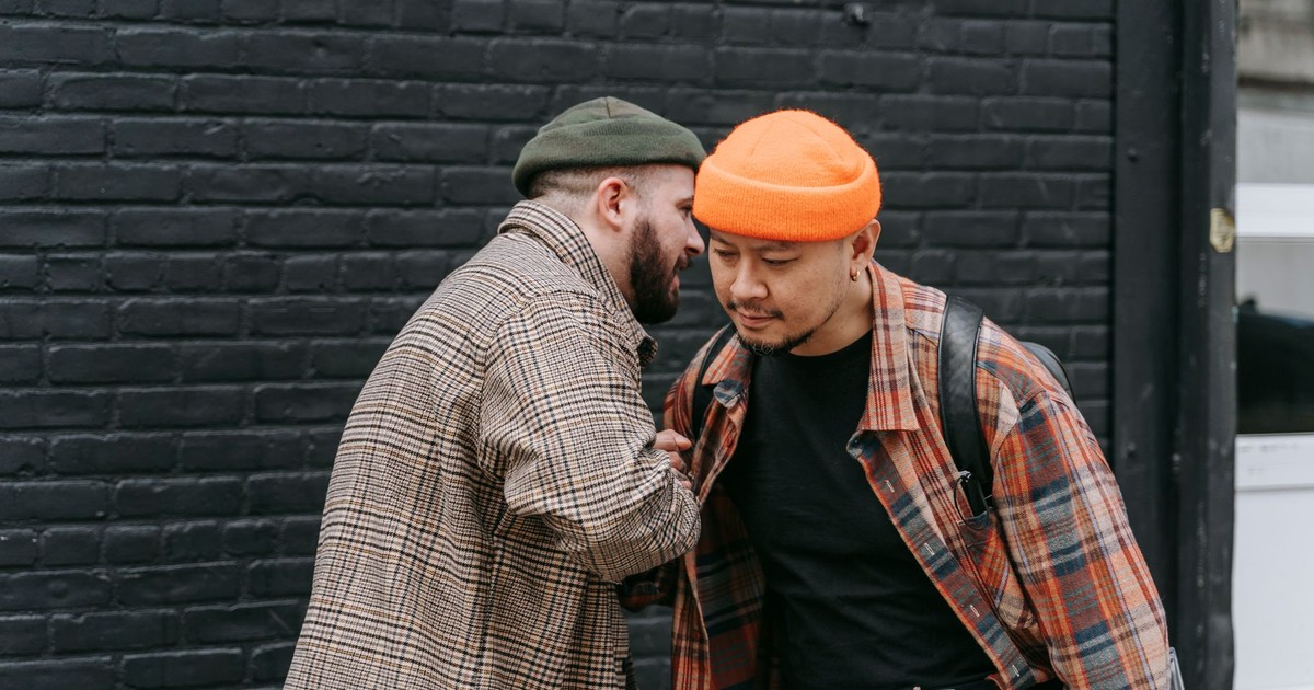 Two men having a casual conversation outdoors, dressed in plaid jackets and beanies.