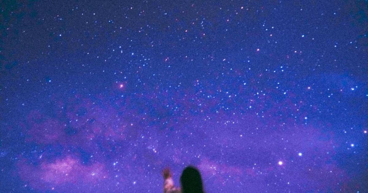 A silhouette of a person reaching towards a vivid starry night sky, featuring the Milky Way.