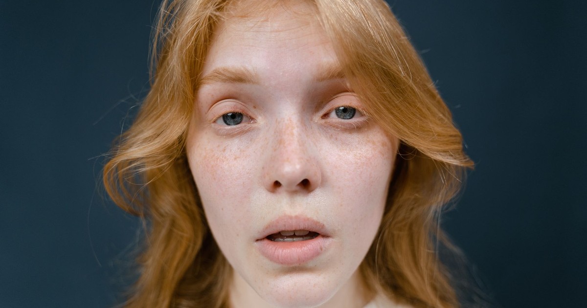 Close-up portrait of a red-haired woman with freckles, exhibiting a natural expression.