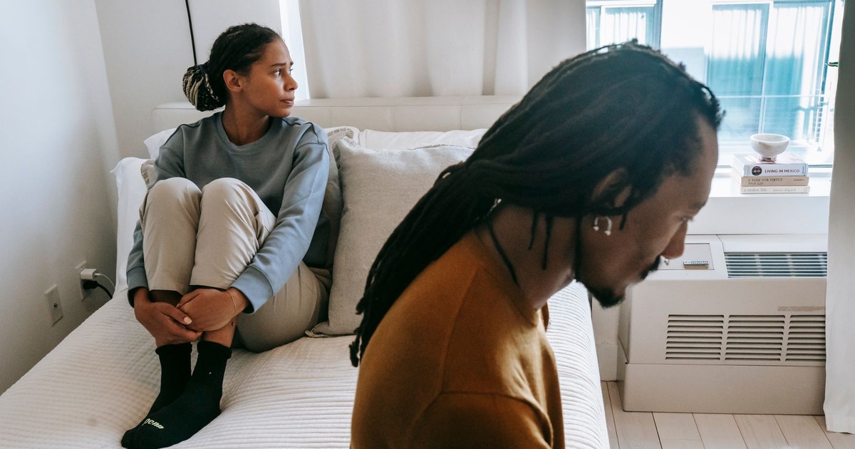 Young African American couple in casual clothes resting on bed with sad face in daytime