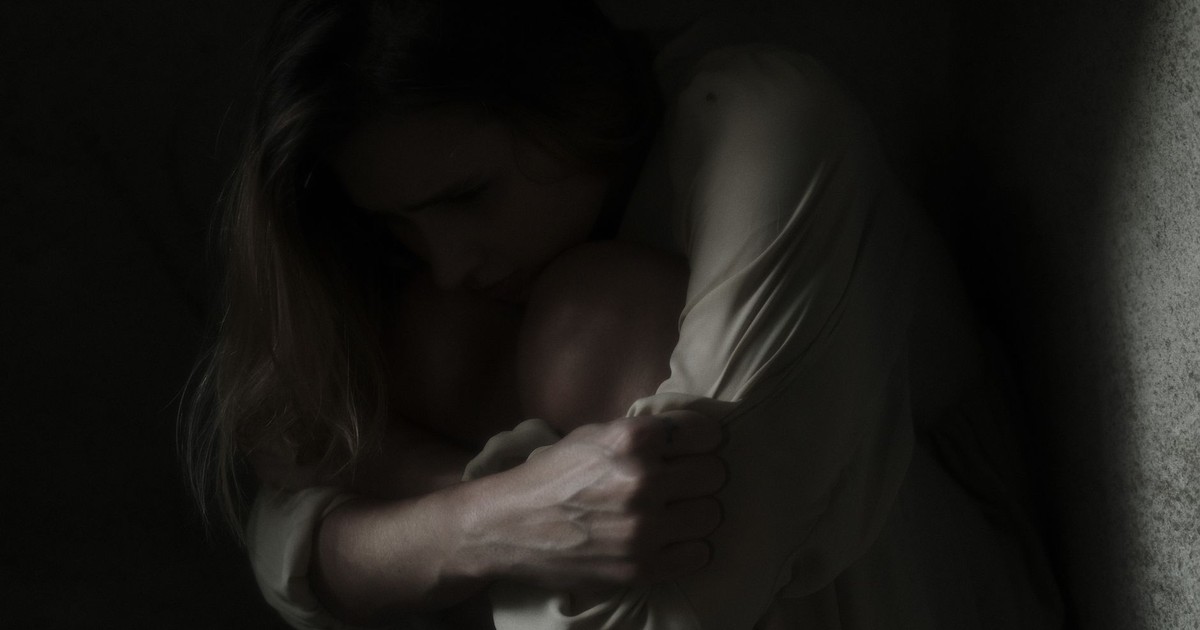 A woman sits in a dimly lit corner, evoking feelings of solitude and introspection.