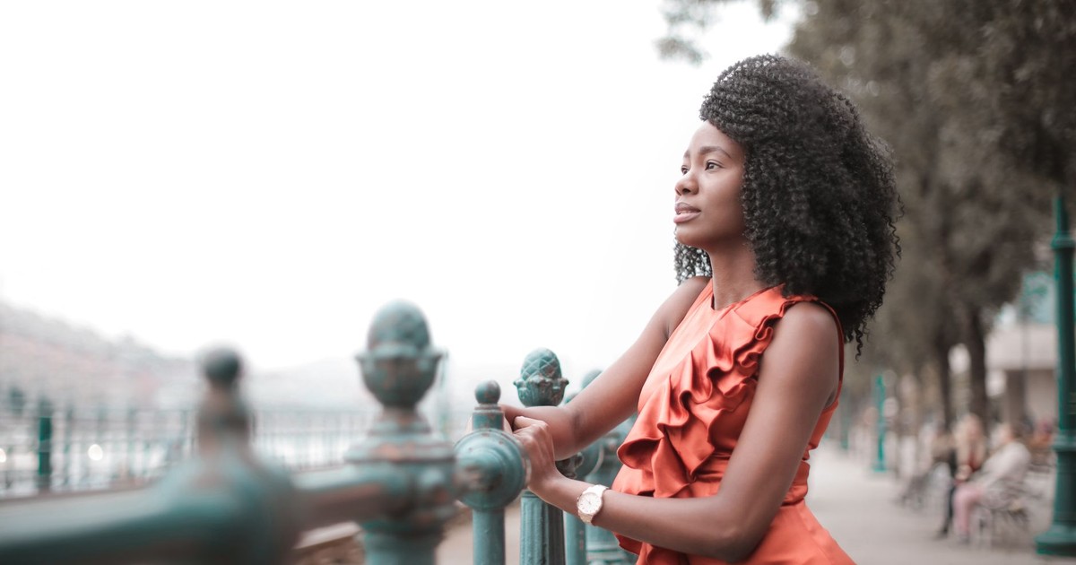 Elegant woman standing by a railing in an orange dress, outdoors.