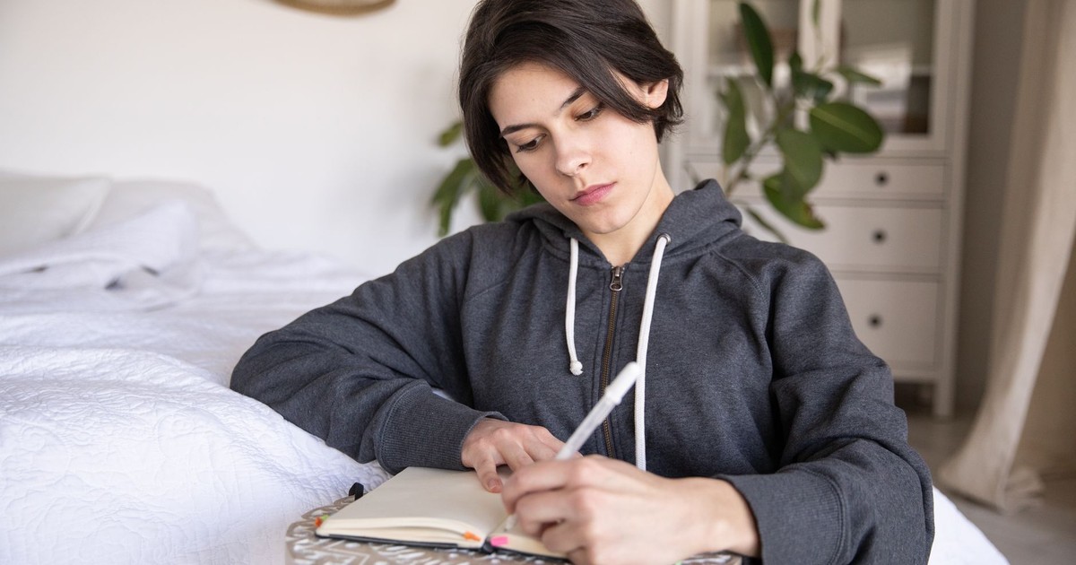 Young woman in a hoodie writing in a notebook at home, capturing a reflective moment.