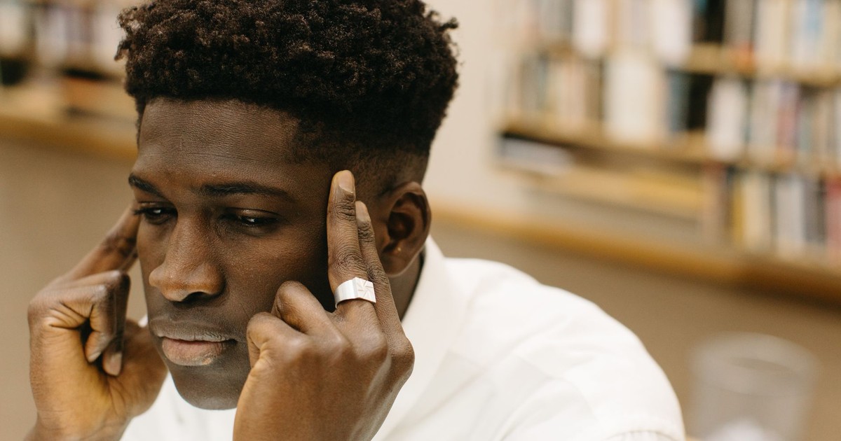 A contemplative man with fingers on temples, pondering in a library.