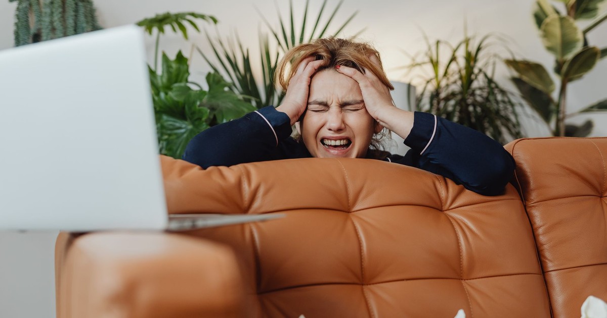 A frustrated woman with eyes closed, sitting on a sofa, experiencing stress at home.