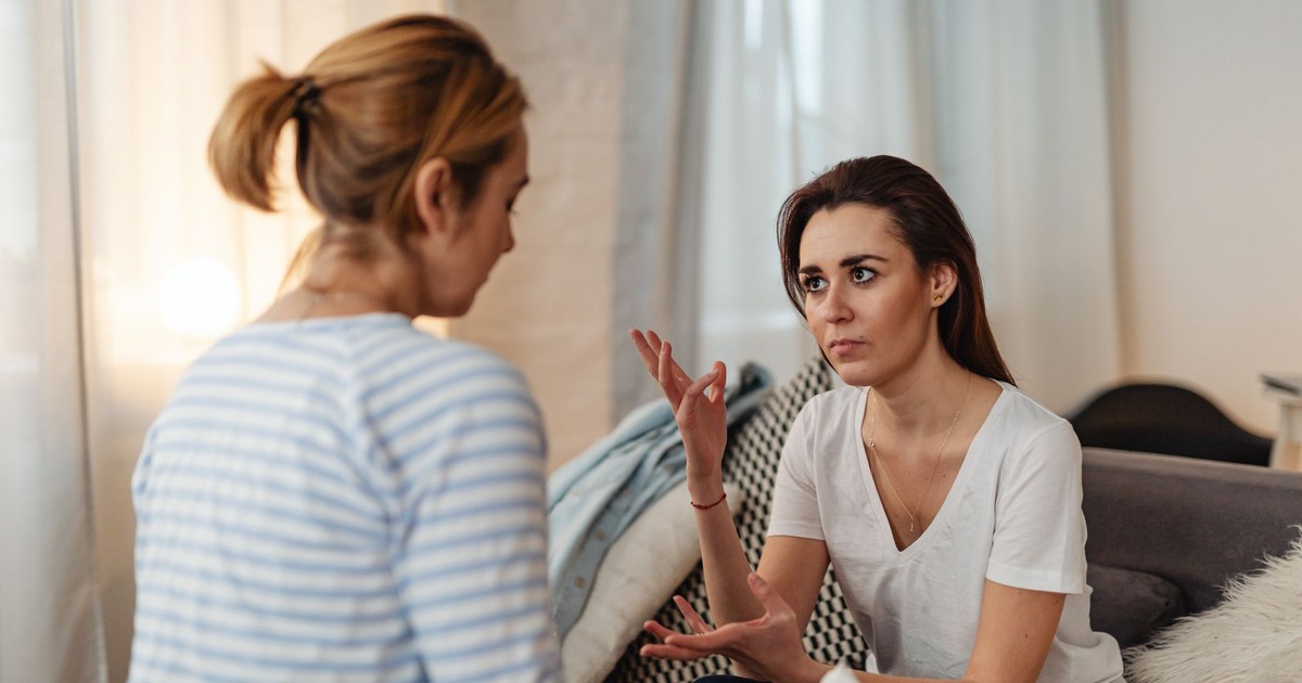 Two women sitting on a sofa, engaged in a serious discussion at home.