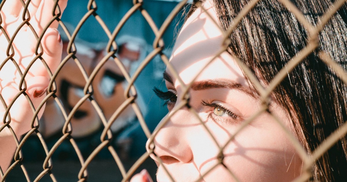 Close-up of a woman looking through a chain link fence capturing natural light.