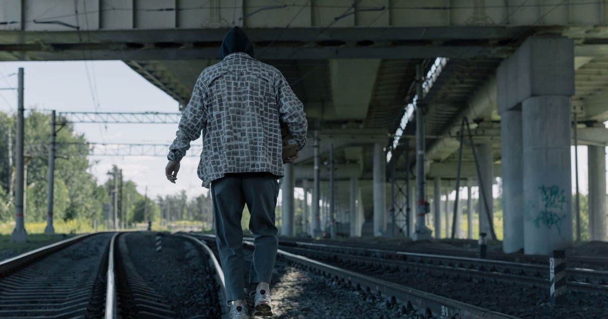 A person walking on railway tracks beneath a large bridge, showcasing urban exploration.