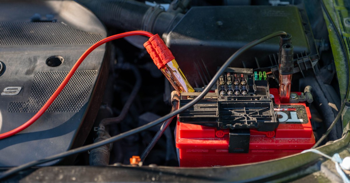 Close-up of a car battery with attached jumper cables in an engine bay.