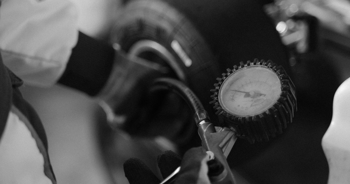 Black and white image of a mechanic using a gauge to check tire pressure on a kart wheel.