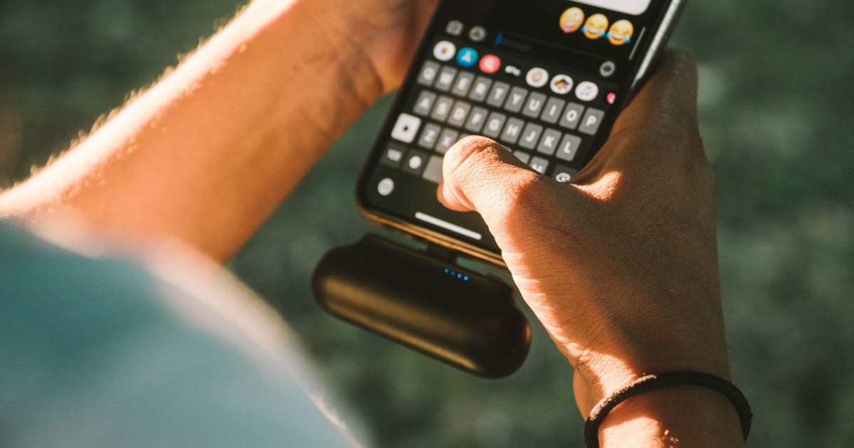 Close-up of a person texting on a smartphone connected to a power bank outdoors.