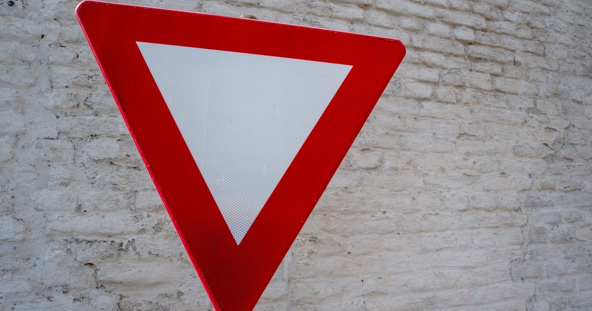 Close-up of red yield traffic sign against a textured white brick wall.
