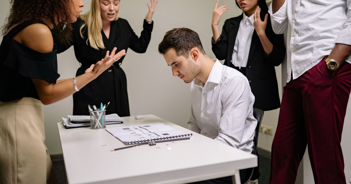 A team confronts a stressed colleague at a tense office meeting, highlighting workplace dynamics.