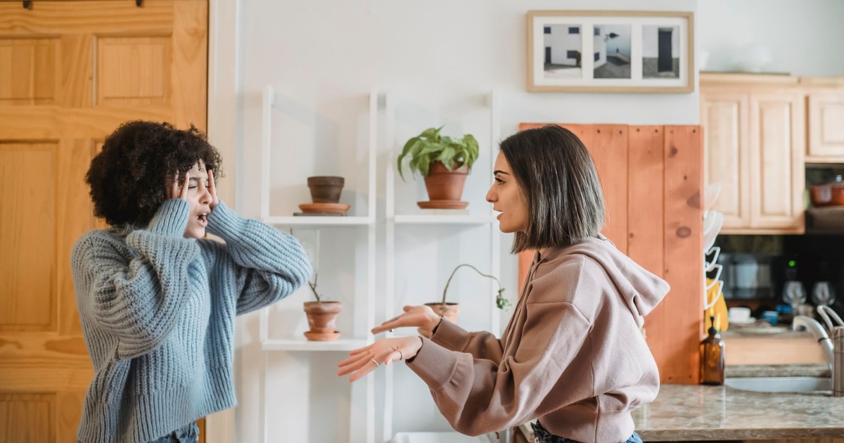 Side view of African American woman with closed eyes quarreling with female wile standing in light room near kitchen at home