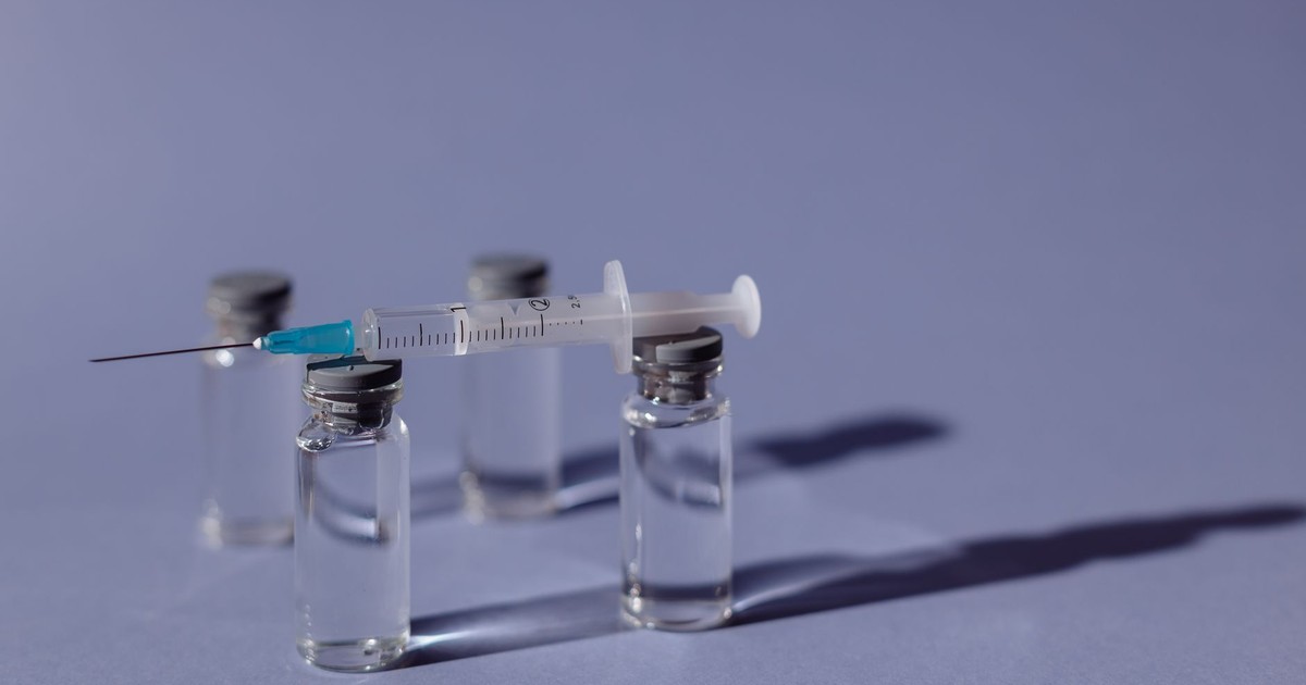 A syringe balanced on vaccine vials with a purple backdrop, representing medical treatment.