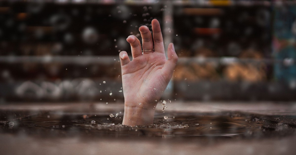 A single hand emerges from water, symbolizing a cry for help amidst a rainy setting.